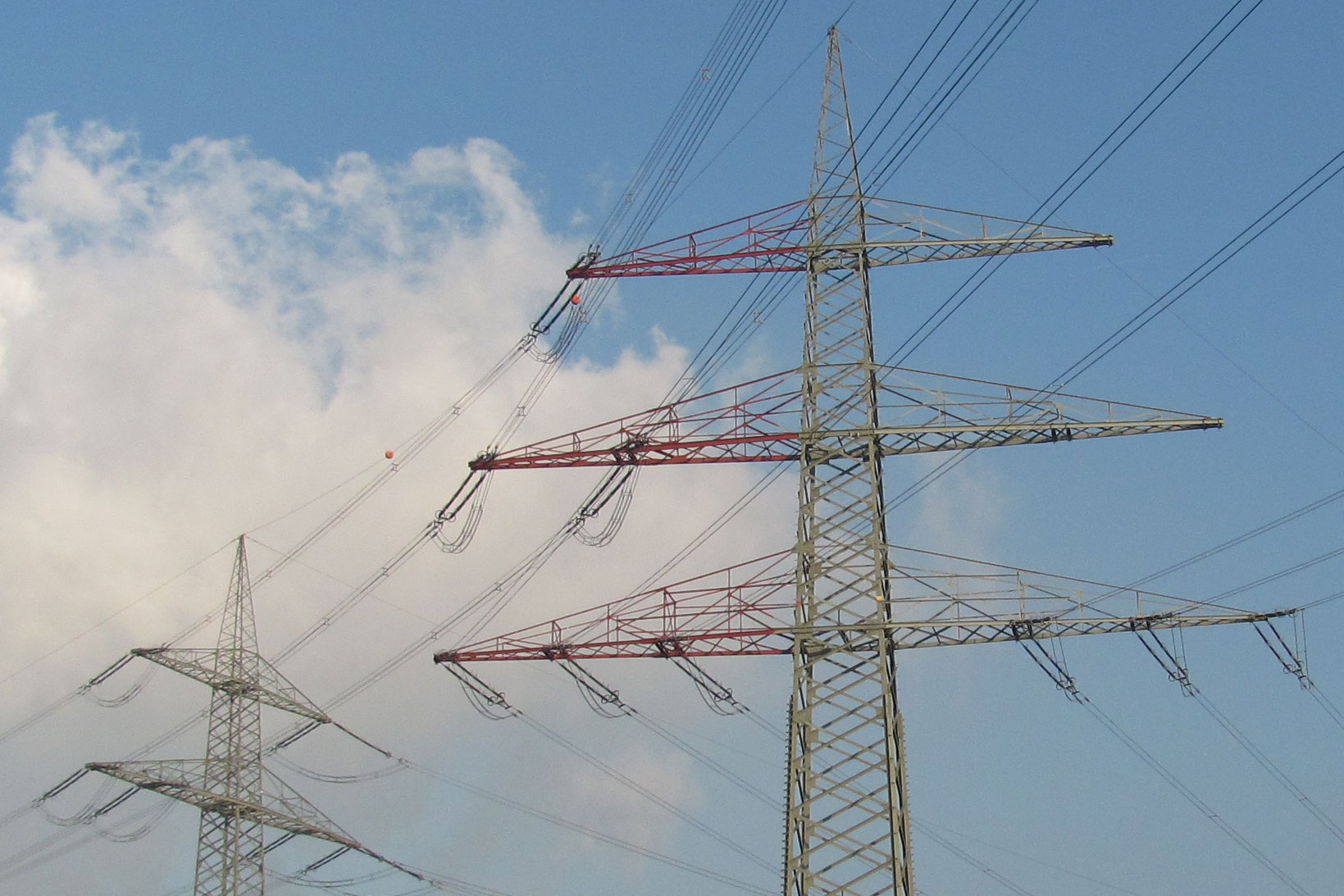 Zwei Strommasten vor leicht bewölktem Himmel